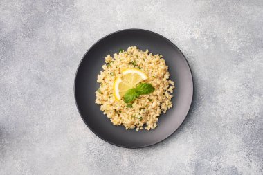 Kaynamış bulgur taze limon ve naneli bir tabakta. Tabouleh Gri Beton Arkaplan Görünümü adında geleneksel bir doğu yemeği, boşluğu kopyala