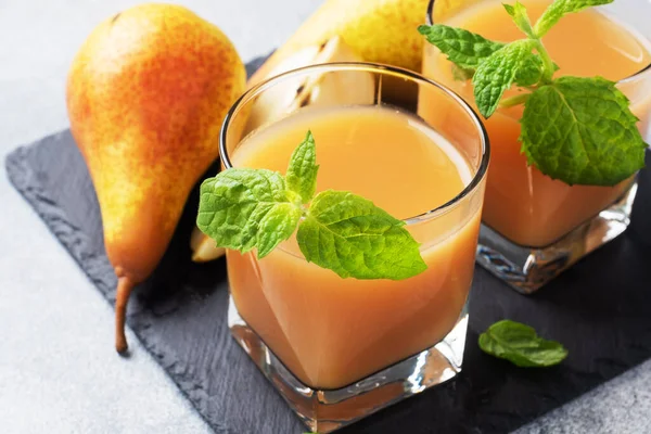 Natural pear juice in a glass cup. Juicy ripe conferences pears and mint leaves Slate stand, light concrete background.
