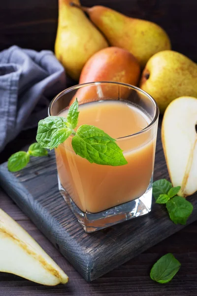 Natural pear juice in a glass cup. Juicy ripe conferences pears and mint leaves Dark rustic wooden background.