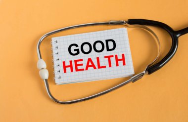 Yazılı Not: Good Health, turuncu arka planda steteskop ile yatar. Tıbbi konsept fotoğrafı
