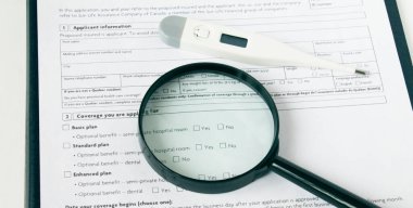Sağlık sigortası formunda bir büyüteç ve elektronik termometre var. Tıbbi konsept