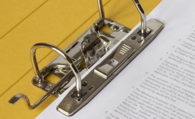 Sarı klasörü kapat, beyaz kağıtlar yığını ve parlak metal halkalar, arka planda odak dışı siyah metin