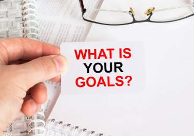 Hedeflerinin ne olduğu yazılı bir kartviziti tutan adamın eli. Gözlüklü ve metin belgeli not defteri. İş konsepti