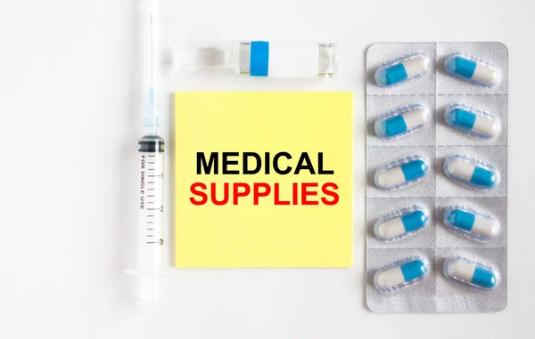 Yellow sticker with text Medical Supplies on a white background with syringes, pills and ampoule. Medical concept photo