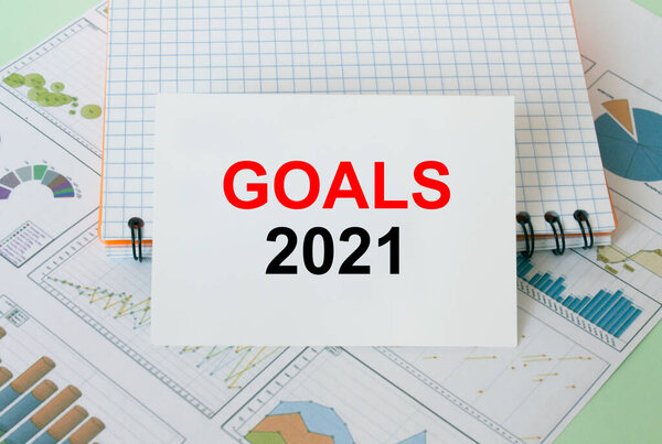 Визитная карточка с текстовыми Целями 2021 на финансовых графиках с блокнотом