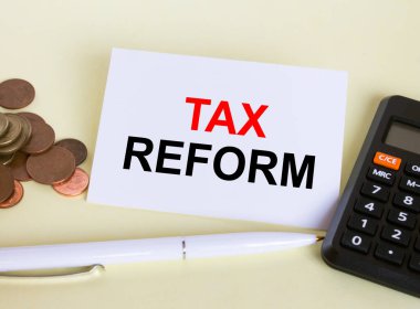 Beyaz kalem hesap makinesi ve bozuk paralarla uzanan Vergi Reformu yazılı kartı ziyaret et