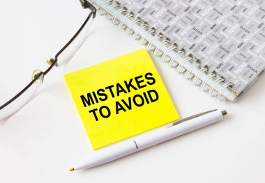 Text Mistakes To Avoid on a yellow sticker lying near notepad with eyeglasses and pen. Could be for business, financial and marketing concepts