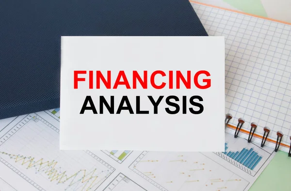 Business card with text Financing Analysis laying on financial graphs with notepad