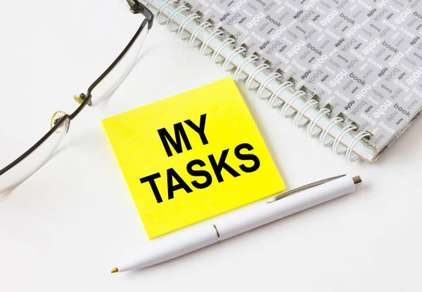Gözlük ve kalemle not defterinin yanında duran sarı bir çıkartmaya görevlerimi yaz. İş, mali ve pazarlama kavramları için olabilir.