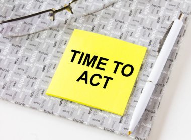 Gözlük ve kalemle not defterine yapıştırılmış sarı bir çıkartmayla harekete geçme zamanı. İş, mali ve pazarlama kavramları için olabilir.