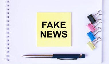 Beyaz bir not defterinde ataç ve ataçla sahte haber mesajı olan sarı etiket. pgoto kavramını