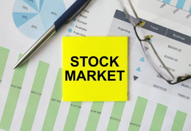 Yellow sticker with text Stock Market lies on financial charts with pen and eyeglass. Financial and business concept
