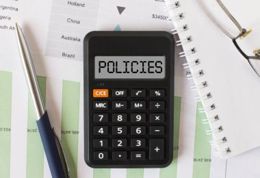 Calculator with the word Policies on the display. Pen, eyeglasses and notepad on the diagrams. Concept photo
