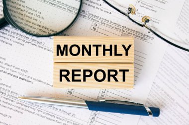 Finansal dokümanların aylık raporlu tahtadan bloklar. Not defteri, büyüteç gözlük ve mavi kalem.