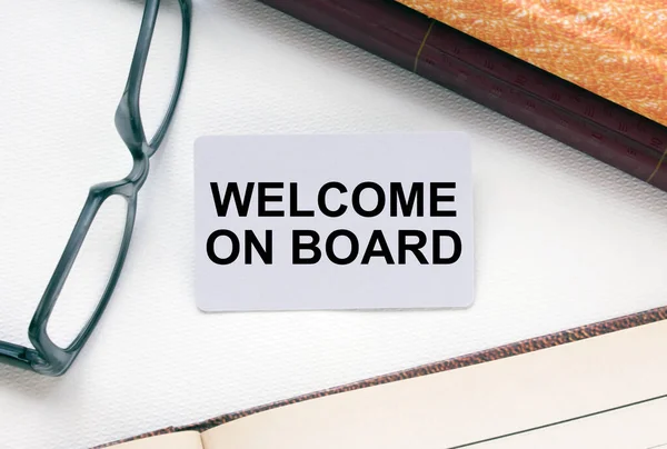 Text Welcome On Board on a business card lying next to notepad with eyeglasses and text documents. Business concept
