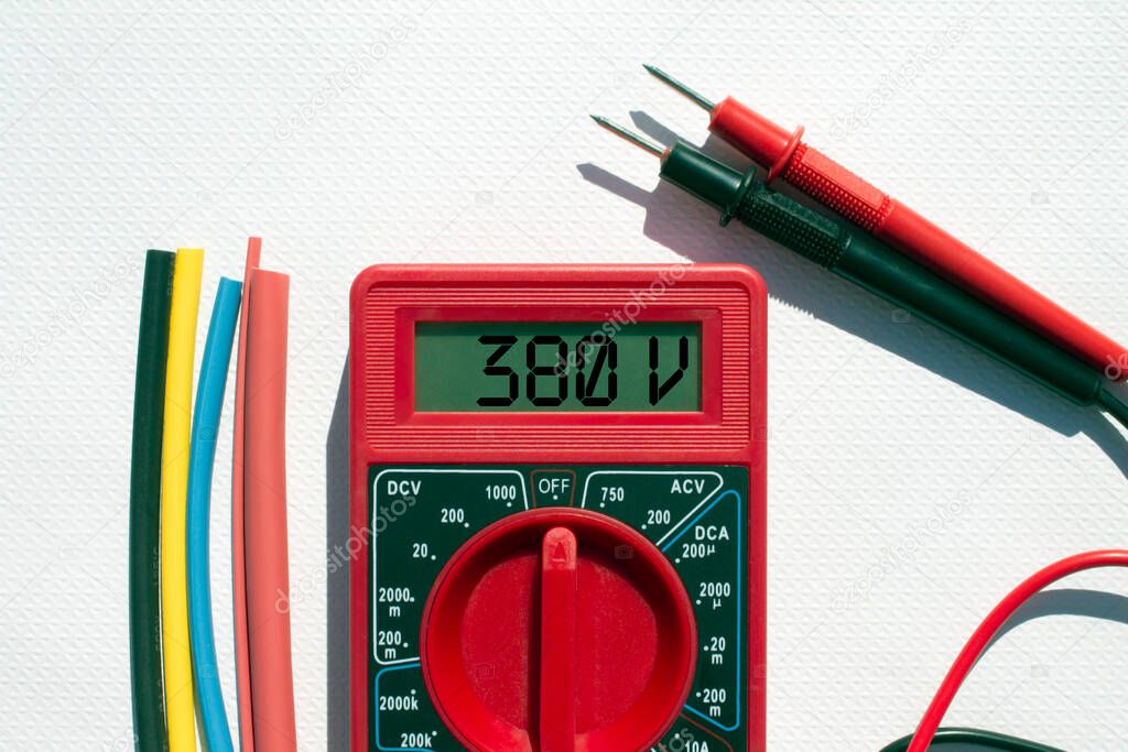 Multimeter with text on display 380 V and heat shrink insulation on white background. Construction and repair