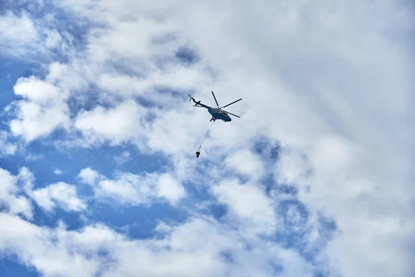 Fire fighting helicopter with water bucket on the background of a cloudy sky