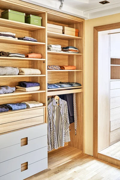 Internal details of the wooden wardrobe with slide out rack for coathangers. Modern wardrobe with clothes hanging on slide out racks and folded on the shelves. Modern furniture