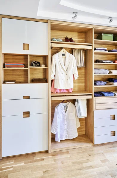 Internal details of the wooden wardrobe with slide out rack for coathangers. Modern wardrobe with clothes hanging on slide out racks and folded on the shelves. Modern furniture