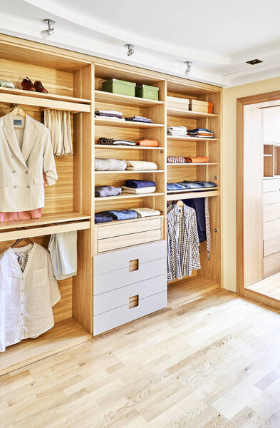 Internal details of the wooden wardrobe with slide out rack for coathangers. Modern wardrobe with clothes hanging on slide out racks and folded on the shelves. Modern furniture