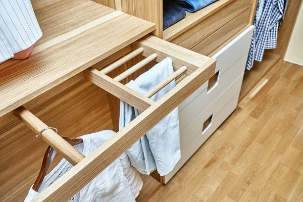 Internal details of the wooden wardrobe with slide out rack for coathangers. Modern wardrobe with clothes hanging on slide out racks and folded on the shelves. Modern furniture