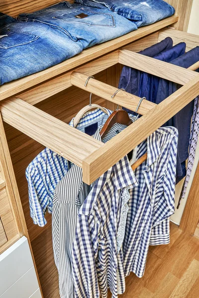 Internal details of the wooden wardrobe with slide out rack for coathangers. Modern wardrobe with clothes hanging on slide out racks and folded on the shelves. Modern furniture