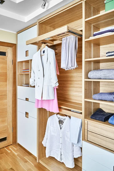 Internal details of the wooden wardrobe with slide out rack for coathangers. Modern wardrobe with clothes hanging on slide out racks and folded on the shelves. Modern furniture