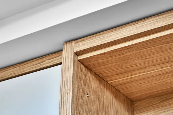 Detail of the wardrobe close-up. Modern wooden wardrobe with flat finger pull wardrobe doors. Oak veneered plywood cabinets with light gray painted cabinet doors. Modern furniture