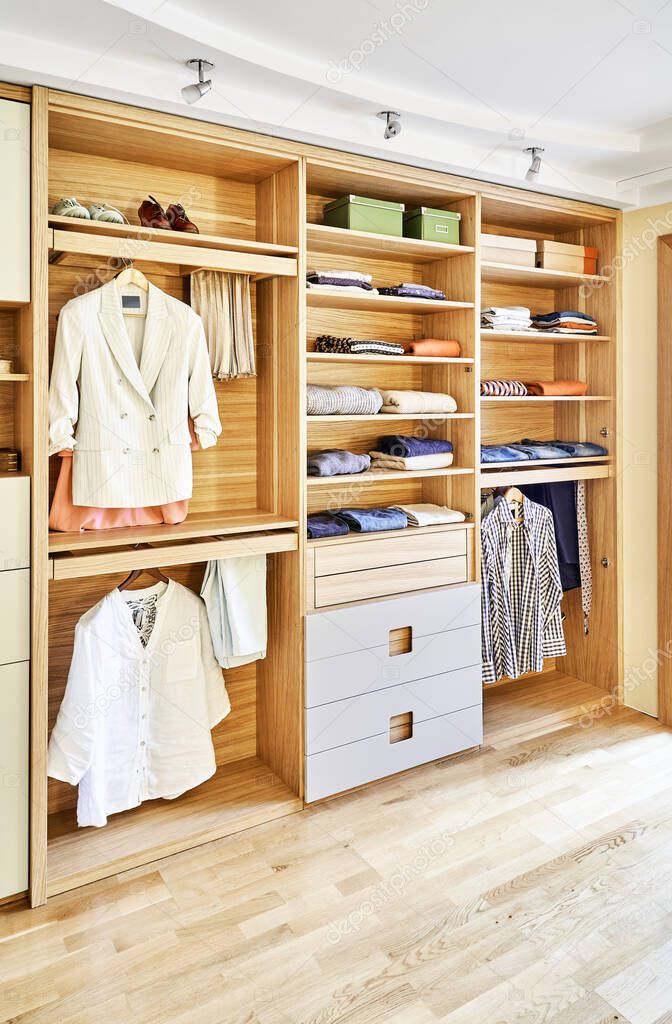 Internal details of the wooden wardrobe with slide out rack for coathangers. Modern wardrobe with clothes hanging on slide out racks and folded on the shelves. Modern furniture