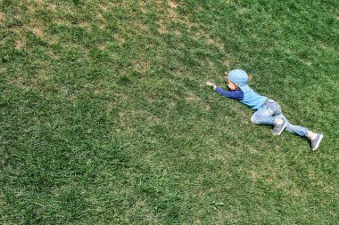 Mavi şapkalı oyuncu çocuk, güneşli bir günde bahar parkında yemyeşil çimlerle kaplı dik yamaçlara çıkar.