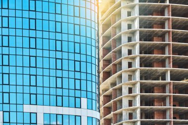 Çağdaş gökdelen binası. Mavi cam cepheli ve gökdelenli. Gün batımında açık inşaat sahasında yüksek bir iskelet.