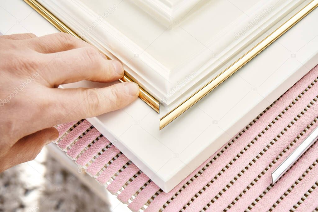 Employee glues elegant golden molding decorative strip on furniture white facade panel in classical style in workshop extreme closeup