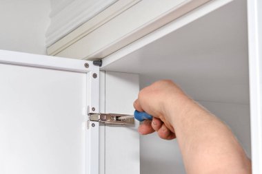 Becerikli tamirci, mobilyaları ayarlar. Menteşeleri, ışık odasına çağdaş beyaz bavul monte eden tornavidayla ayarlar.