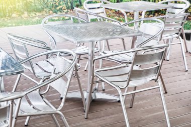 Günümüzün modern boş metal masaları ve sandalyeleri güneşli bir günde, yaz kafeteryasının ahşap terasında duruyor.