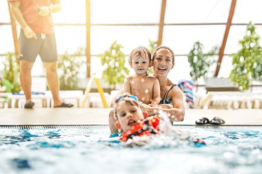 Joyful young mother with cute little sons has fun swimming and playing in large pool with clear water at city sports complex