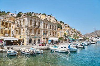 Symi, Yunanistan - 05 Temmuz 2017: Güneşli bir günde Yunanistan 'ın Suriye adasındaki eski bir kasabada tarihi binalara karşı mavi deniz yatlarına demirlenmiş tekneli liman