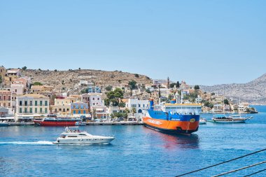 Symi, Yunanistan - 05 Temmuz 2017: Yunanistan 'ın Suriye adasındaki tepelere dağılmış çok renkli eski binalarla tarihi kente karşı büyük bir yelken feribotu demirledi