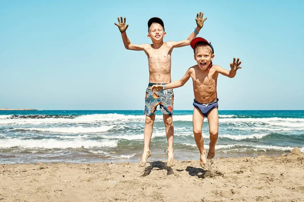面白い喜びの弟でショートパンツビーチでジャンプします 湿った砂対紺碧の海の波と青い空夏の日にPrasonisiの岬 — ストック写真