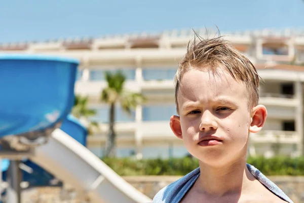 晴れた日に熱帯リゾートのウォータースライドの近くにタオルで面白い少年の肖像画 — ストック写真