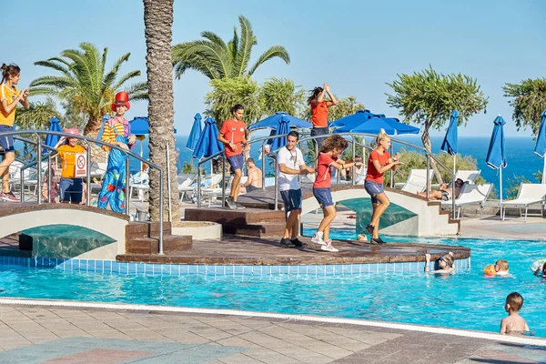 Rhodes, Yunanistan - 29 Haziran 2017: Yaratıcı genç animasyonculardan oluşan bir ekip, güneşli bir günde tropikal tatil beldesindeki büyük açık yüzme havuzu yakınında ve köprülerde dans ediyor