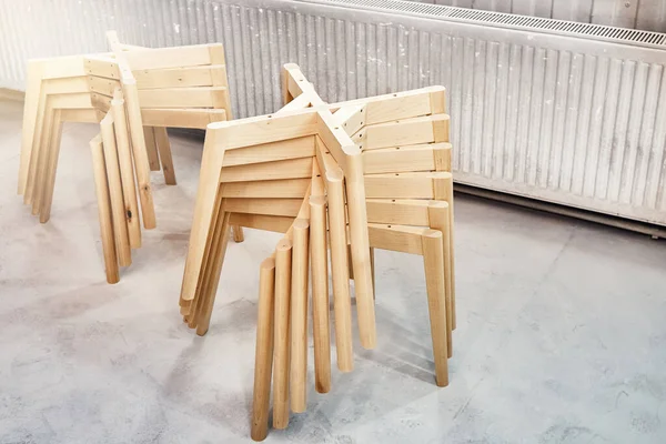 Stacks of new wooden bases with simple legs for elegant chairs assembling in light paint spraying booth at workshop closeup