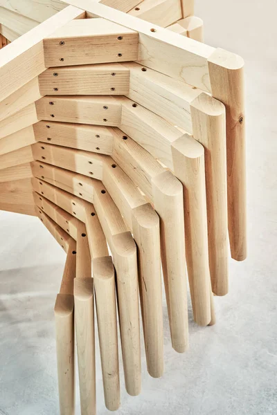 Stacks of new wooden bases with simple legs for elegant chairs assembling in light paint spraying booth at workshop extreme closeup