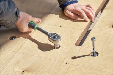 Yetenekli bir zanaatkar, güneşli bir günde büyük bir ahşap yemek masası toplar, ingiliz anahtarıyla vidaları açık havada döndürür.