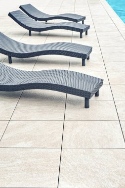 Geri dönüştürülmüş malzemeden yapılmış yeni siyah hasır plastik şezlonglar parlak güneş ışığı altında, havuz kenarında, aydınlık fayanslı zemin üzerinde duruyor.