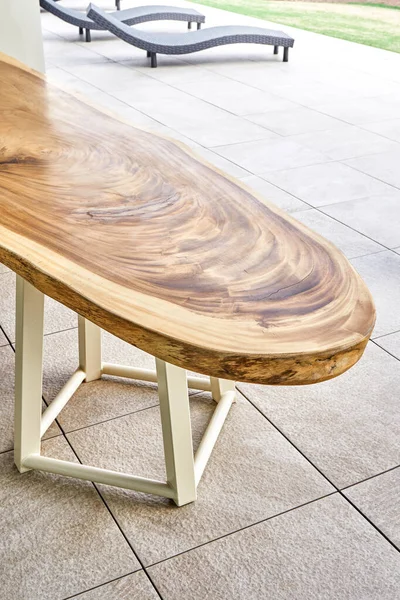 Wonderful designer dining table made of large lacquered live edge suar wood slab on metal carcass stands in yard of elegant cottage closeup