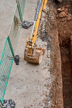 Kovalı renkli kazıcı, çitlerle çevrili yeni su borularını değiştirmek için derin çukurun yanında duruyor.