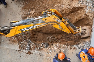 İzhevsk, Rusya - 08 Mayıs 2021: Çağdaş sarı kazıcı, eski çukur kazıyor ve yukarıdan bakıldığında toprak zemine yeni su boruları döşüyor
