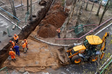 İzhevsk, Rusya - 08 Mayıs 2021: Üniformalı işçiler, bahar günü üst görünümde konut inşaatı sahasında boru hattının değiştirilmesinde kazıcıyla birlikte derin çukurlar kazdılar