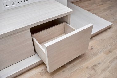 Modern parlak bir odada, ahşap bir kürsüde açık çekmeceleri olan, kaplamalı ve sade ak meşe kerestesinden yapılmış televizyon seti için şık bir tuvalet.