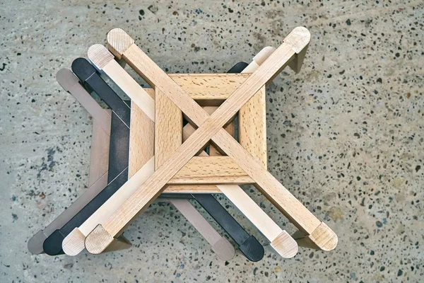 Stack of multicolored wooden bases with legs for elegant chairs on concrete floor at workshop closeup upper view